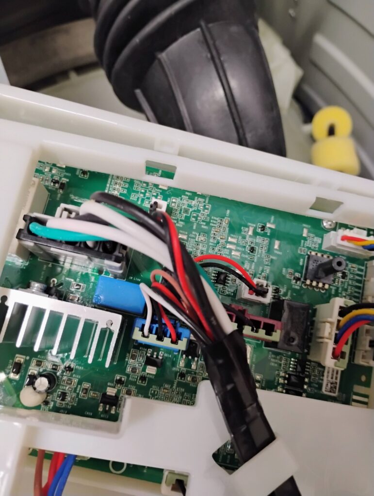 Close-up of an appliance circuit board being repaired by a technician, showing electrical components and connections.