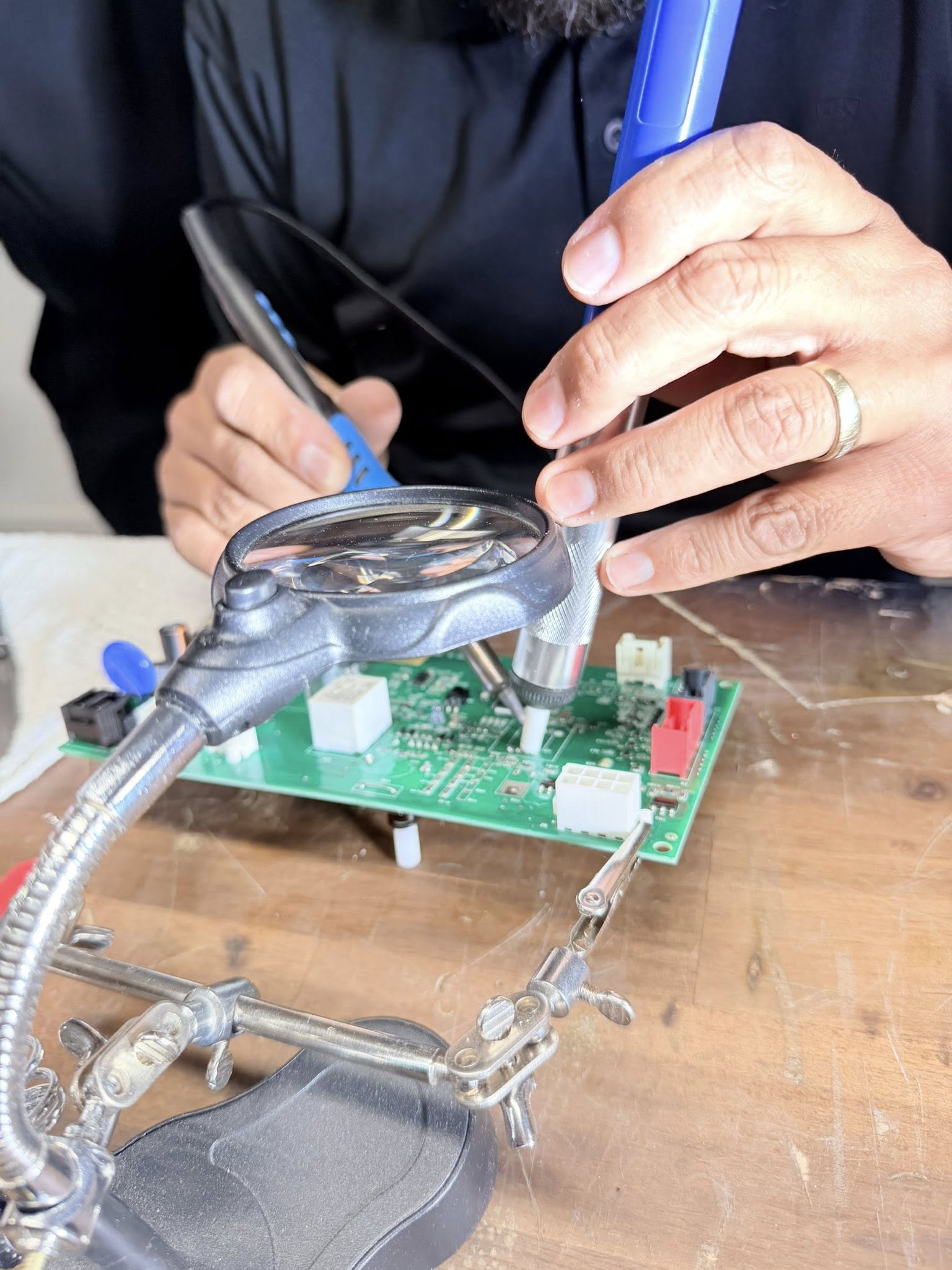 Technician repairing an appliance circuit board with tools, focusing on electrical diagnostics in a workshop.