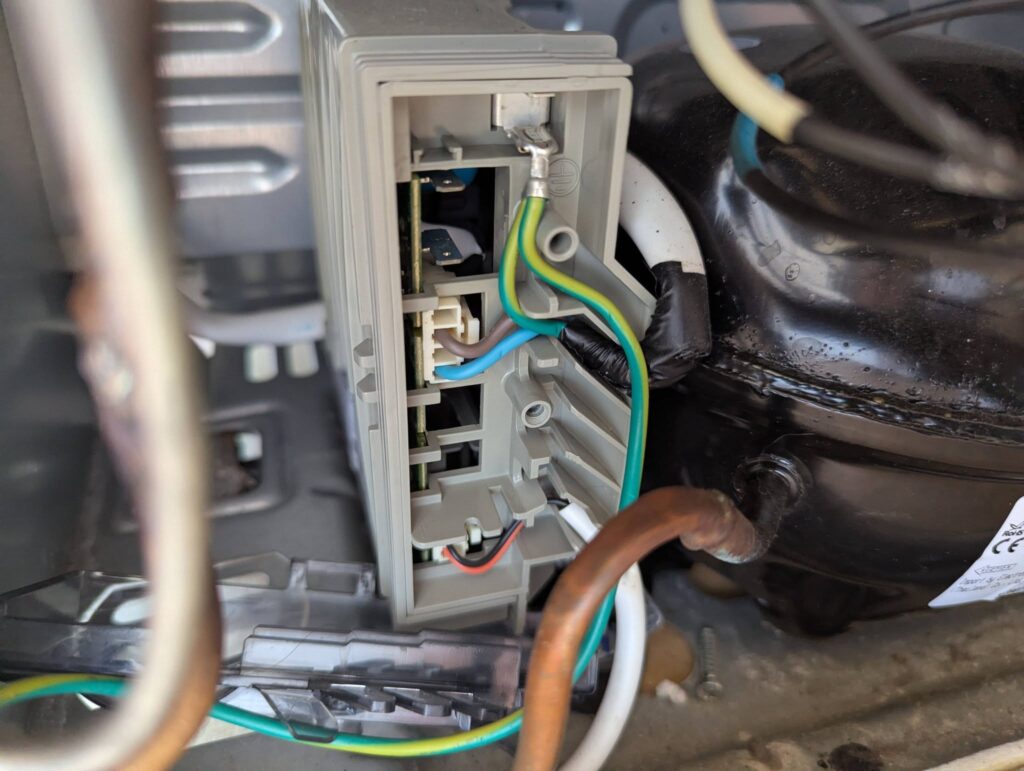 Technician repairing electrical components inside an appliance, focusing on connections and wiring.